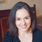 Alexandra Macdonald wearing black, smiling, indoors on wooden bench