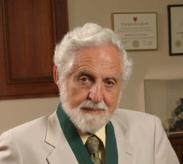 Djerassi wears a tan suit jacket and green ribboned medal around his neck