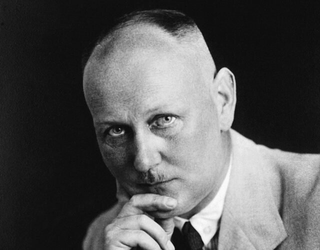 Gerhard Domagk stares towards the camera with his chin resting on his hand. he wears a light colored jacket with a dark tie.