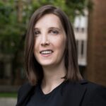 Bree Lohman, wearing black suit, outdoors on a university campus