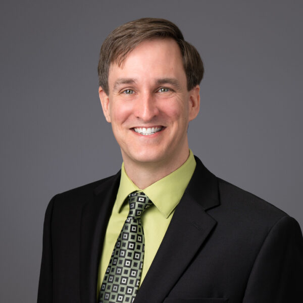 Caleb Funk smiling, wearing black blazer, green dress shirt, tie