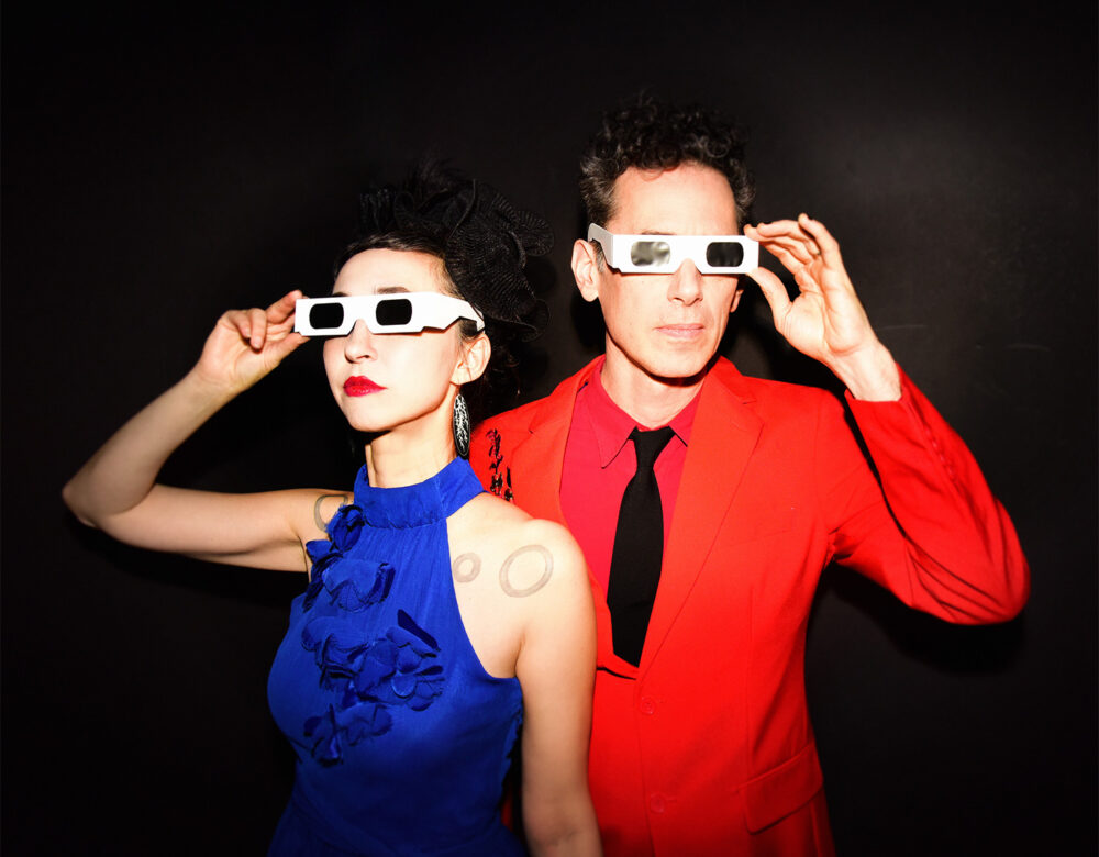 Ellia Bisker and Jeff Morris wearing eclipse glasses in a dark studio