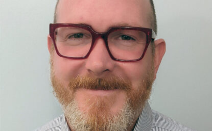 Clay smiling and wearing glasses and a striped shirt