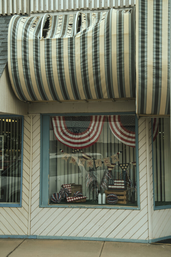 Storefront with a torn awning and an American flag themed display in shop window