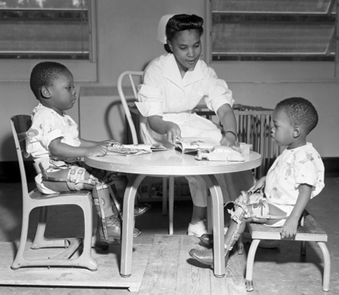 Nurse sitting at a small table with two children in leg braces