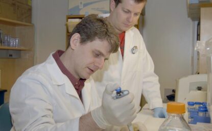 Two scientists in lab coats work in lab.