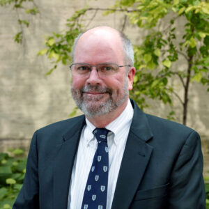 Jim outdoors, smiling, wearing glasses and suit and tie