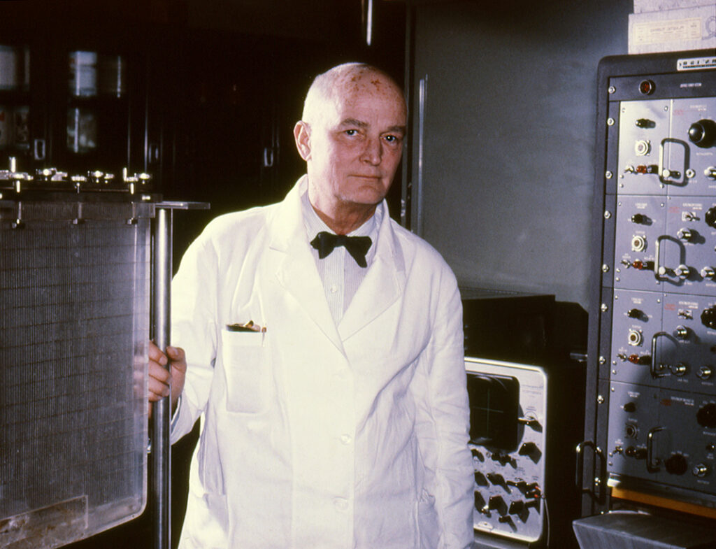 Color photo of older man in lab coat with machine