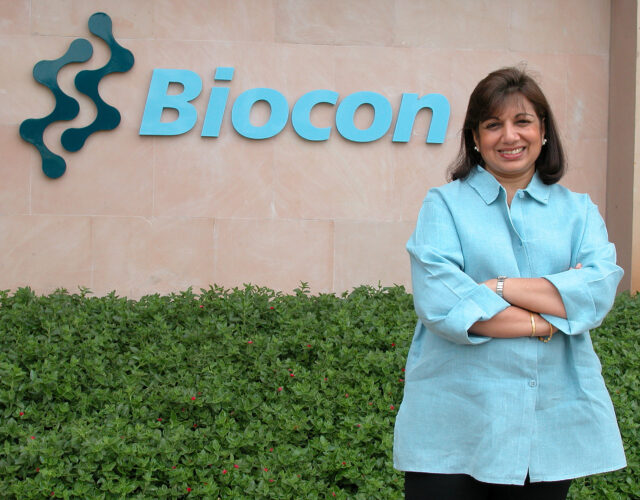 Photo of Kiran Mazumdar-Shaw standing in front of the Biocon building.