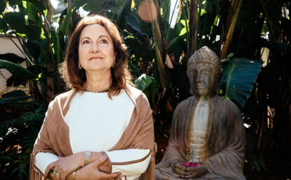 Photograph of Magda Marquet, in a garden, next to a Buddha statue.