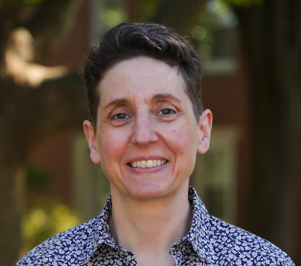 Melanie Nilsson smiling, wearing blue and white patterned collared shirt