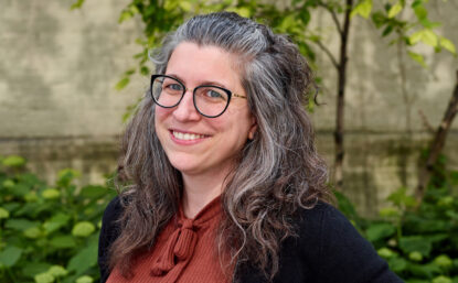 Michelle outdoors, smiling, wearing glasses and terra cotta sweater under black cardigan