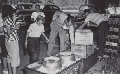 People at a picnic reaching into Coca-Cola coolers filled with ice