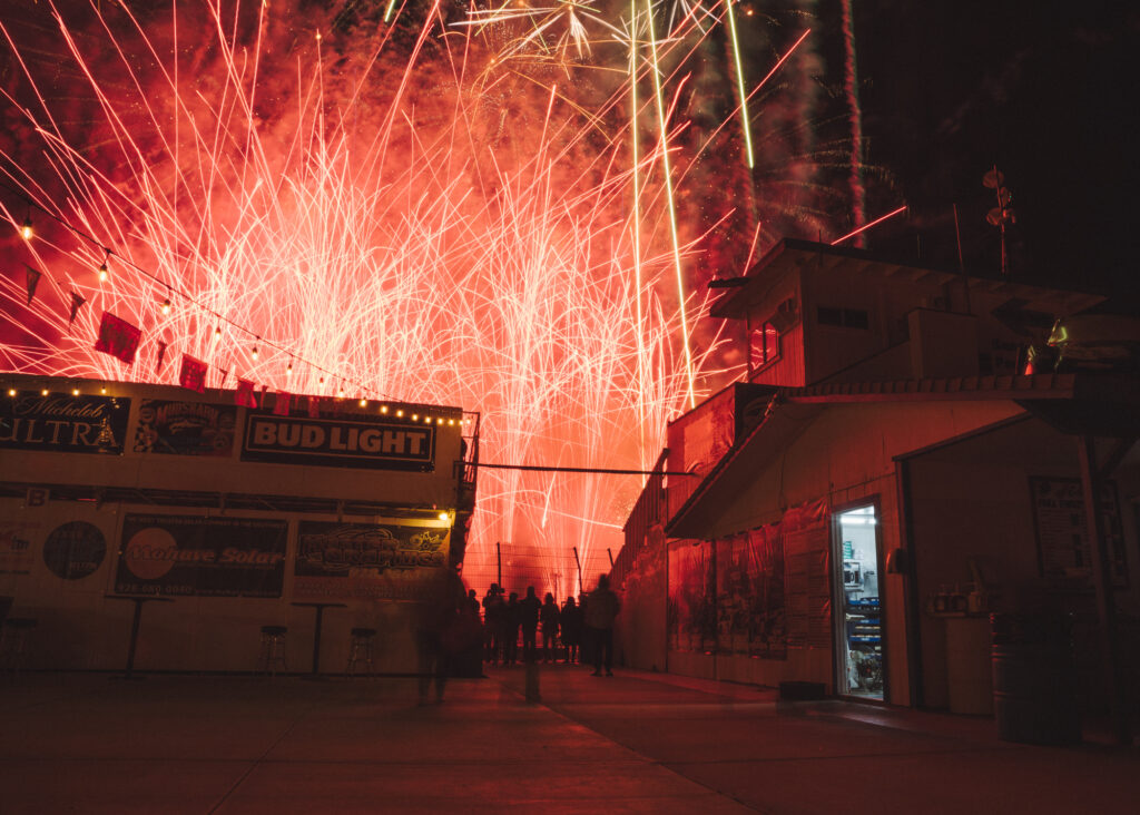 Landscape of red colored fireworks display with dark concession stands in foreground