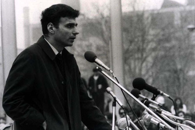 Man speaking in front of microphones outside