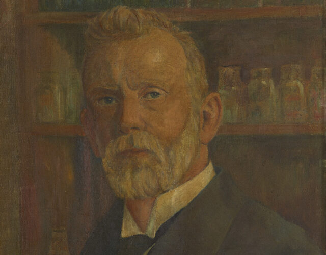 Painting of a older man with a white beard standing in front of shelves of medicine. He appears to be wearing an early 20th century suit.