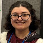 Samantha Nadel, smiling, wearing glasses, maroon and off-white top, blue lanyard