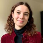 Sara Bassanelli wearing dark red velvet jacket, black shirt, head tilted to her left