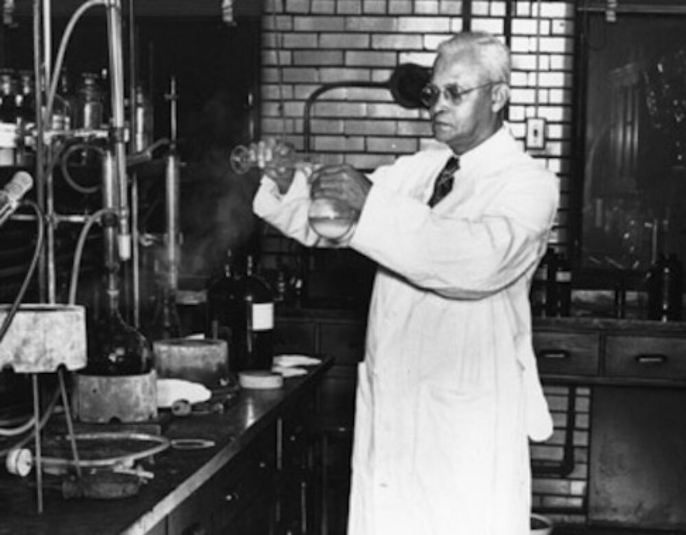 St. Elmo Brady in a chemistry lab at Fisk University. He is pouring a liquid from one beaker into another. There are counters of lab equipment surrounding him.