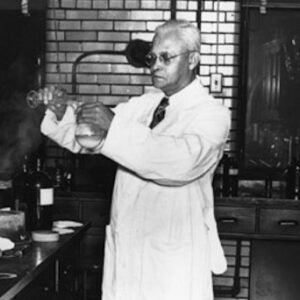 St. Elmo Brady in a chemistry lab at Fisk University. He is pouring a liquid from one beaker into another. There are counters of lab equipment surrounding him.