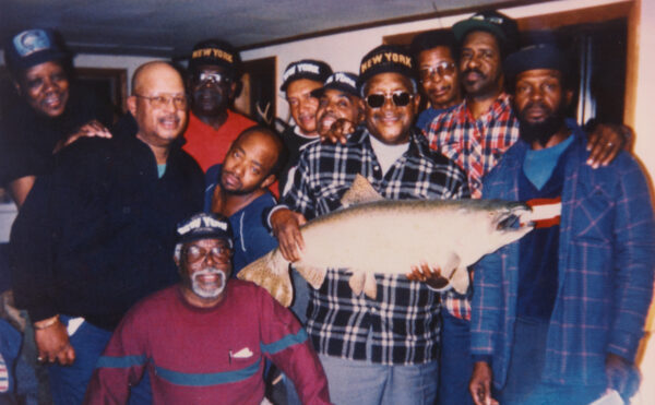 Group of eleven older men posing with a large taxidermy fish