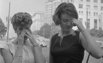 Two women standing on street dabbing their eyes