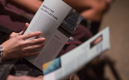 People seated at an event reading a program