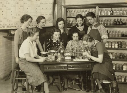 group of women standing around a lab table with periodic table in background