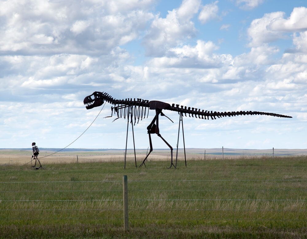 Roadside sculpture showing a skeleton man walking a skeleton dinosaur