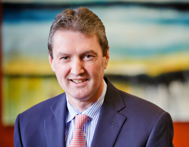 Photograph of Mark Stevenson in blue suit and red tie.